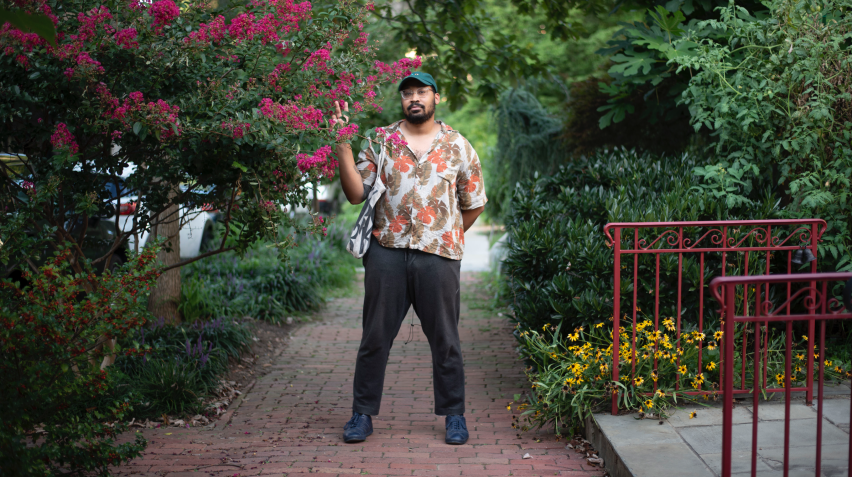 A photo of musician Bartees Strange standing on a sidewalk between trees