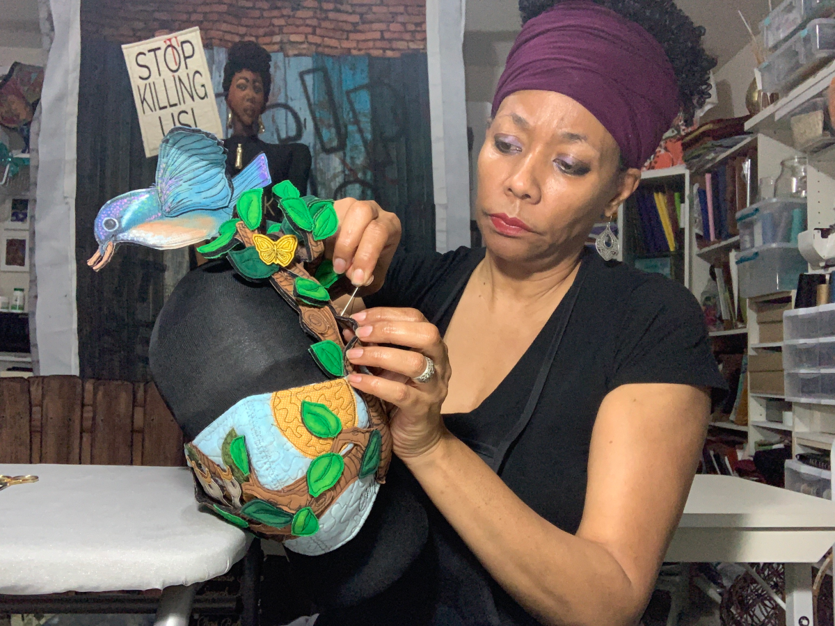 A close up of the artist in her studio making a mask with a motif of leaves, butterflies and birds
