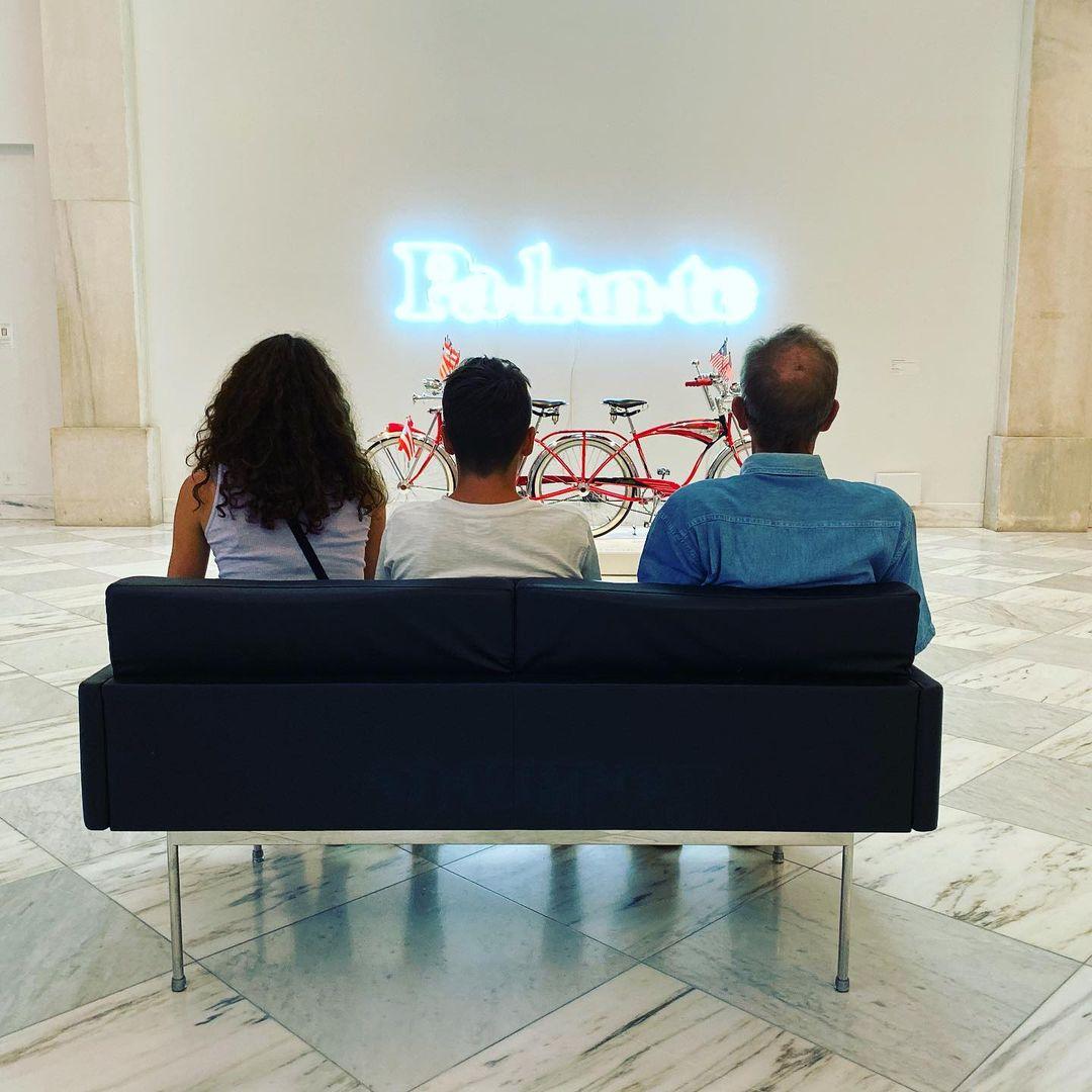 Three people sitting on a sofa looking at neon sign artwork "Pa-lan-te"