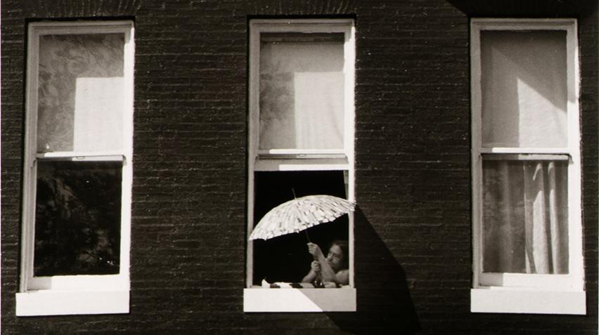 Blog - Welcome Home Introduction, homepage A black and white photograph of a person leaning out of a window, holding an umbrella.