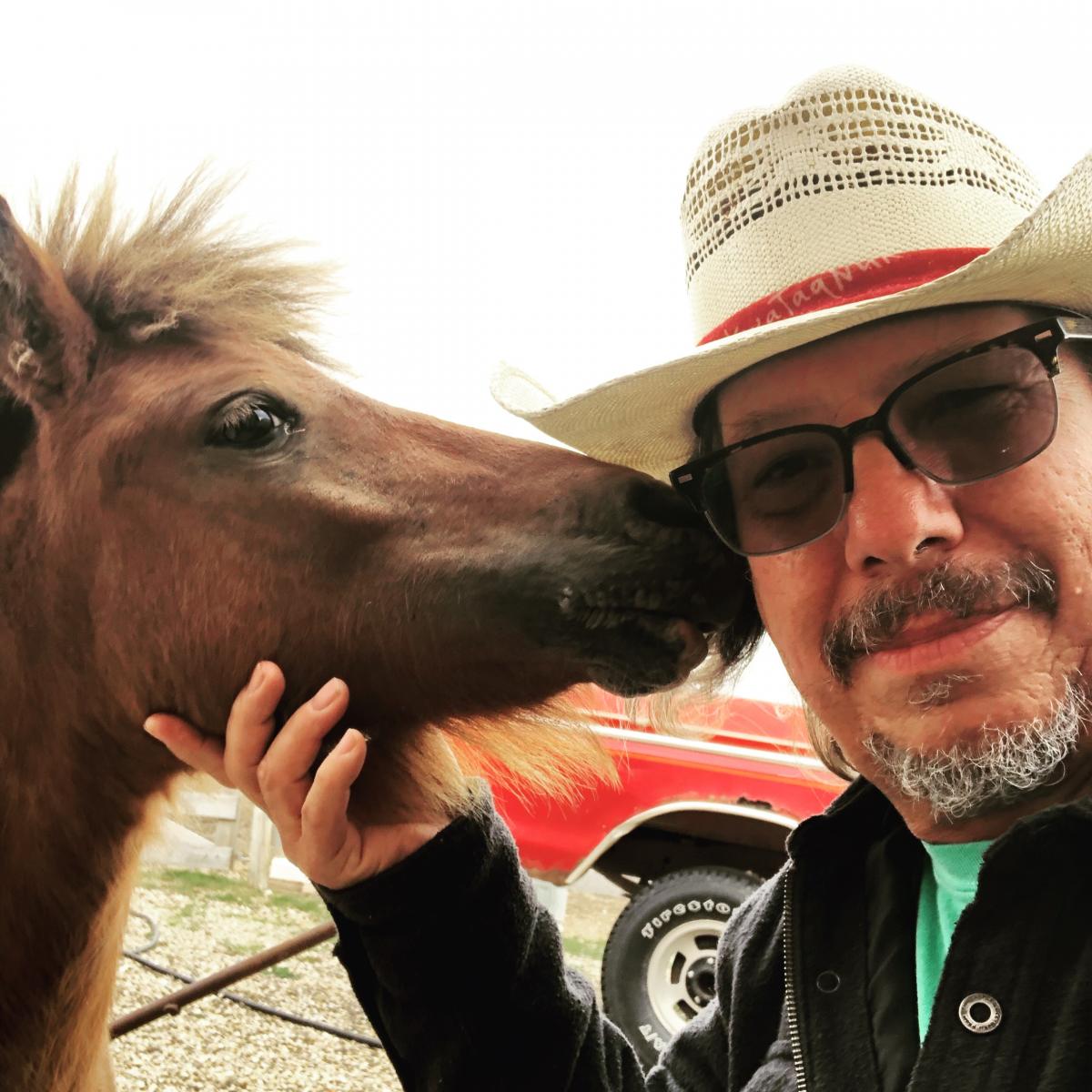 Man with mustache holding horse's head who is trying to lick the side of his face