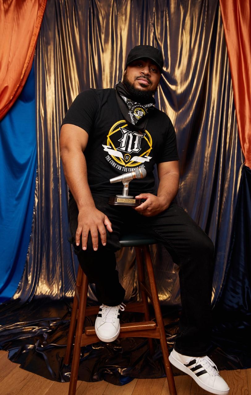 Emcee, Night Train 357, poses with his WAMMIE award in front of a gold curtain.