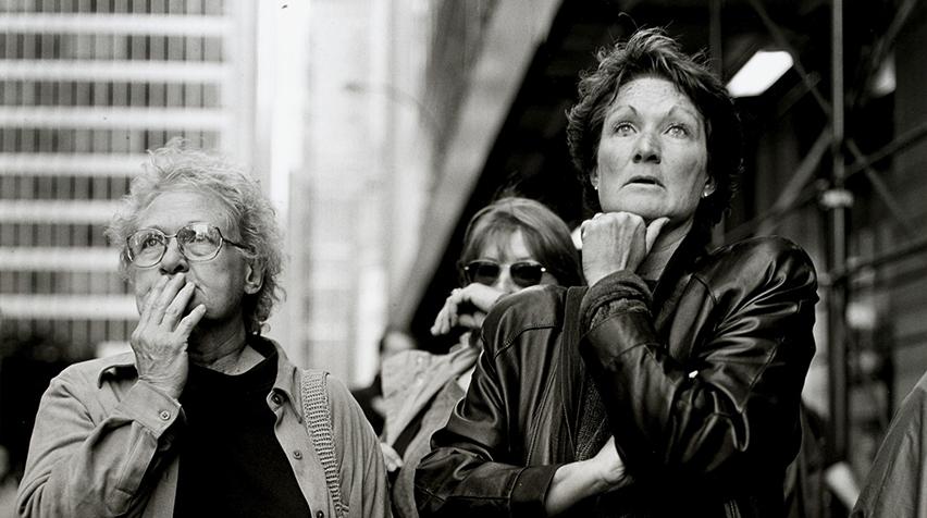 A black and white photograph of three women looking in the near distance with shocked looks on their faces