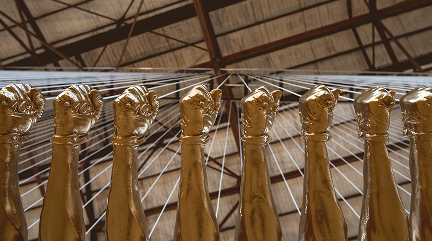 Blog - Glenn Kaino Interview, Bridge, homepage crop A detail of a sculpture of fiberglass fists painted gold