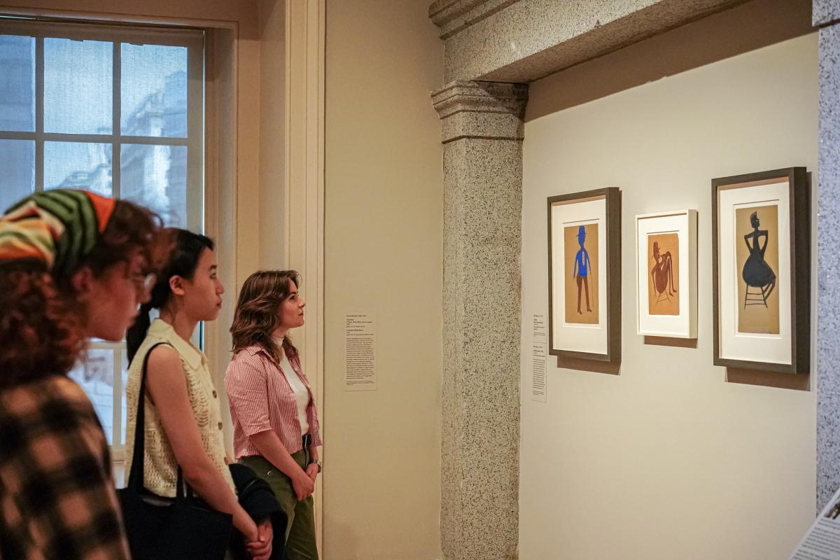 Visitors view three works of Bill Traylor in the exhibition gallery.