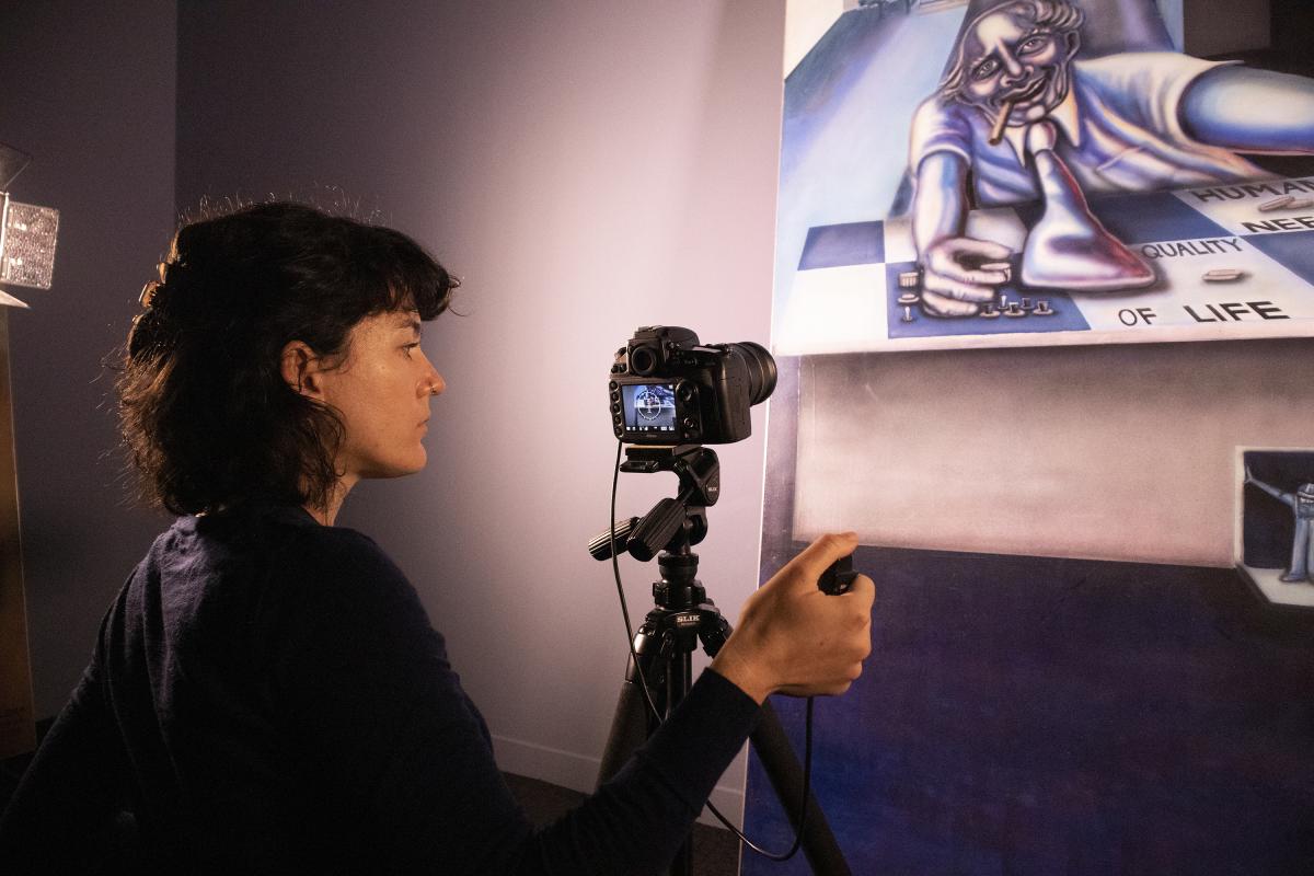 Conservator stands in front of a mural, using a camera on a tripod to capture a detailed photograph.