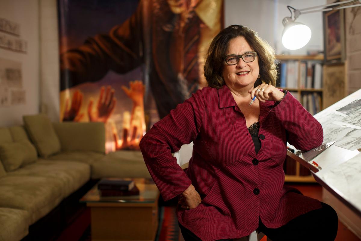 Artist Judy Baca in her home, standing in front of a drawing table.