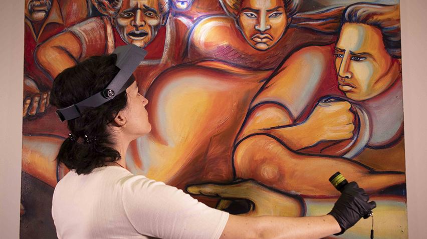 Conservator wearing a head lamp, shines light on a mural.