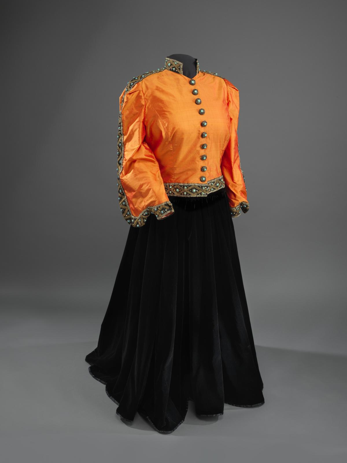 A woman's dress that is orange on top with black buttons and a black skirt.