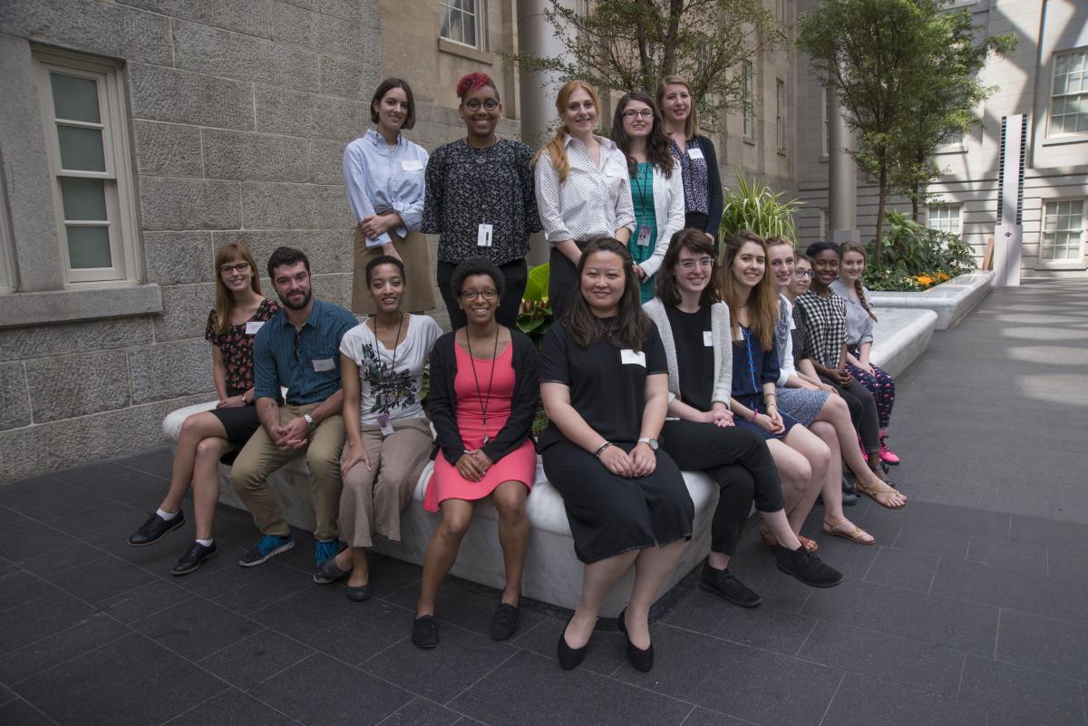 A group of smiling interns sit together in the Kogod Courtyard