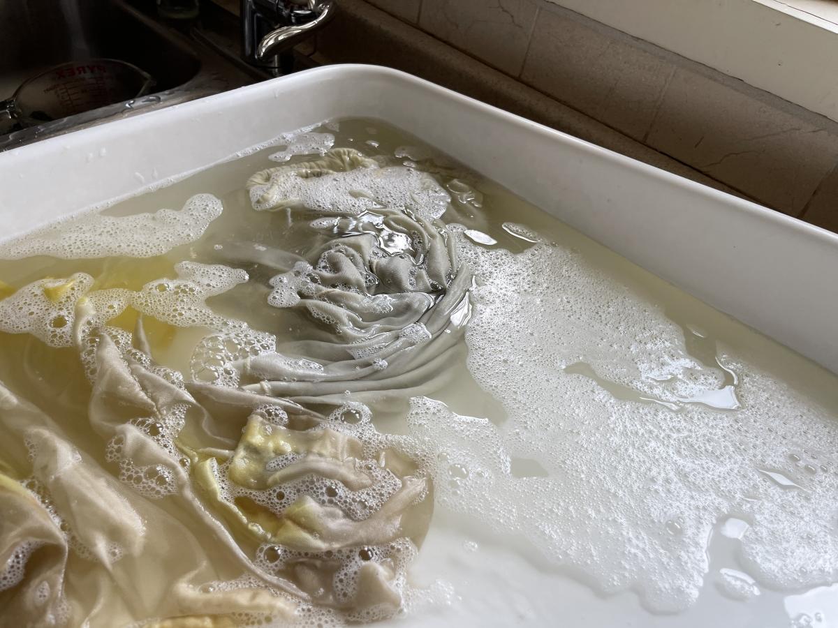 An off-white doll blouse in a wash tub, surrounded by soap suds and dirty water.