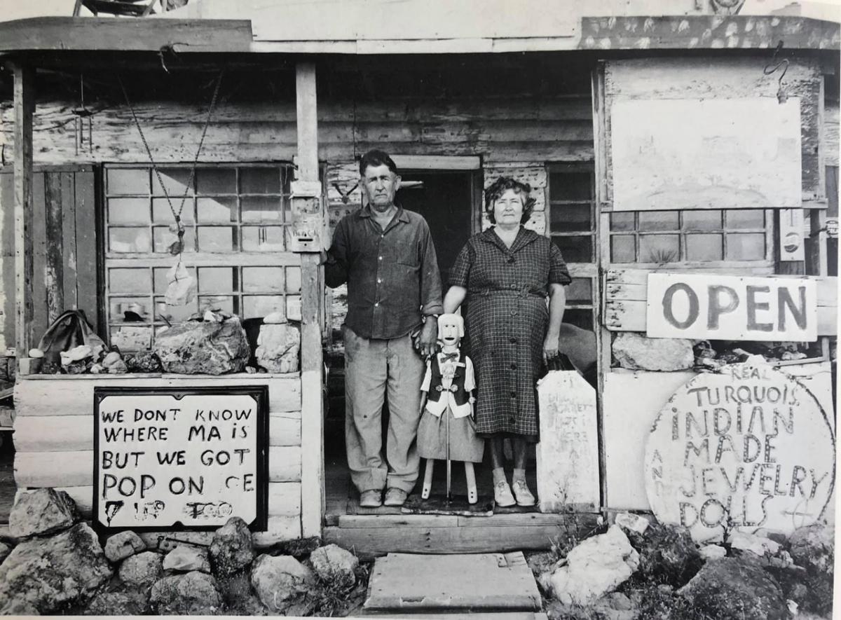 A black and white photograph of a man and a woman standing on a front porch, surrounded by signs.