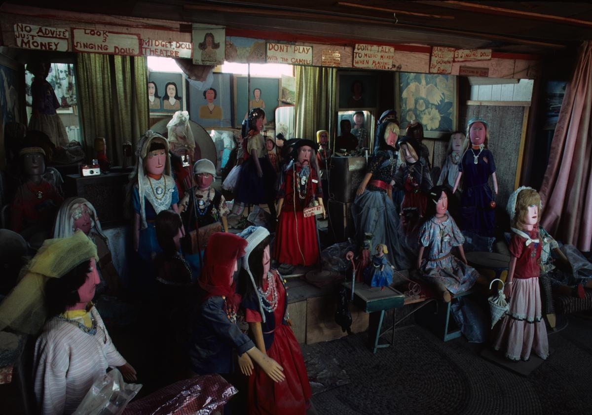Interior photograph of a dimly-lit room filled with large-scale dolls.