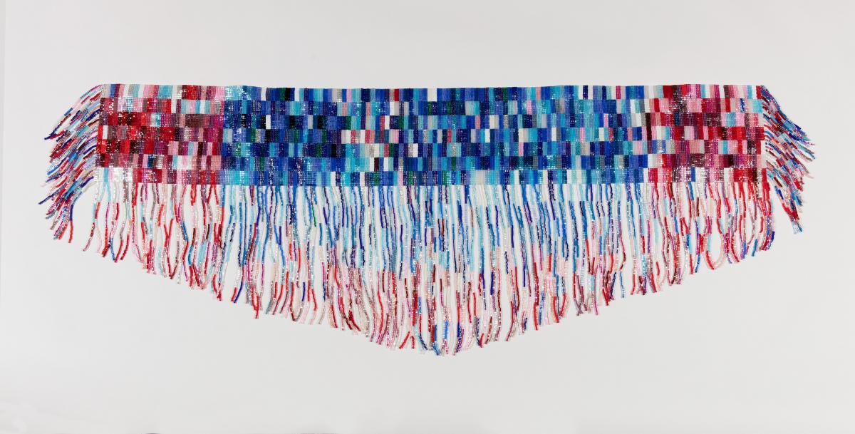 A beaded strap with fringe hanging down the long side. The middle is beaded in blues and both ends are beaded in red hues.