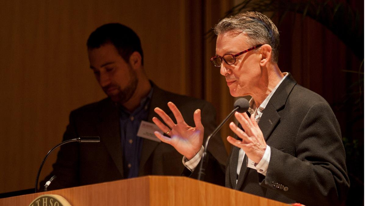 A man lectures in front of a podium