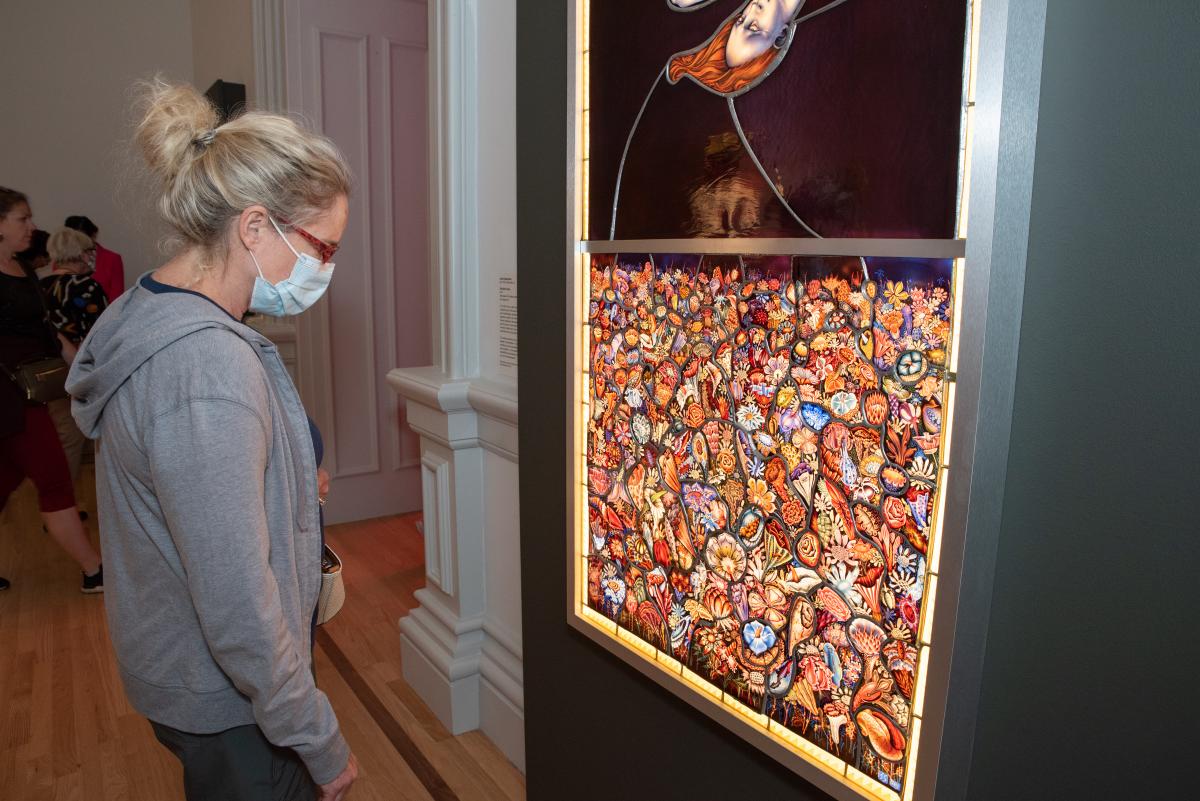 A woman with blonde hair and wearing a face masks looks at the bottom half of "The Birth of Eve"