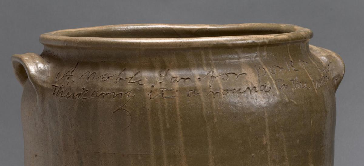 The top of a brown clay pot showing lines of a poem which are inscribed around the opening.