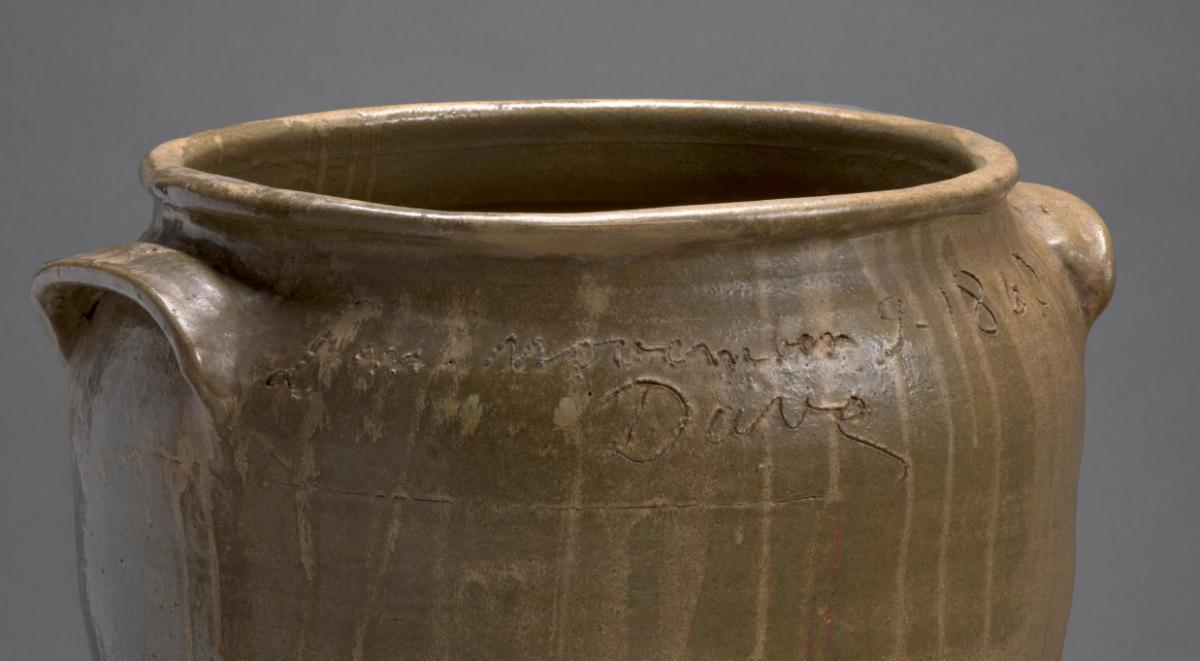 The top of a brown clay pot showing the artist's signature which is inscribed around the opening.