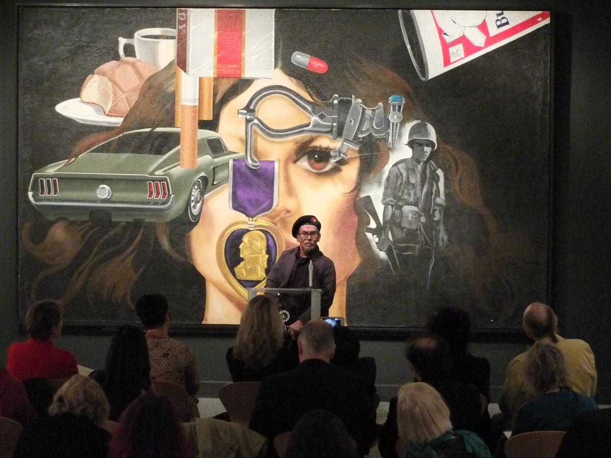 Jesse Treviño speaking at the press preview for Artists Respond: American Art and the Vietnam War, 1965 to 1975 in front of his painting Mi Vida