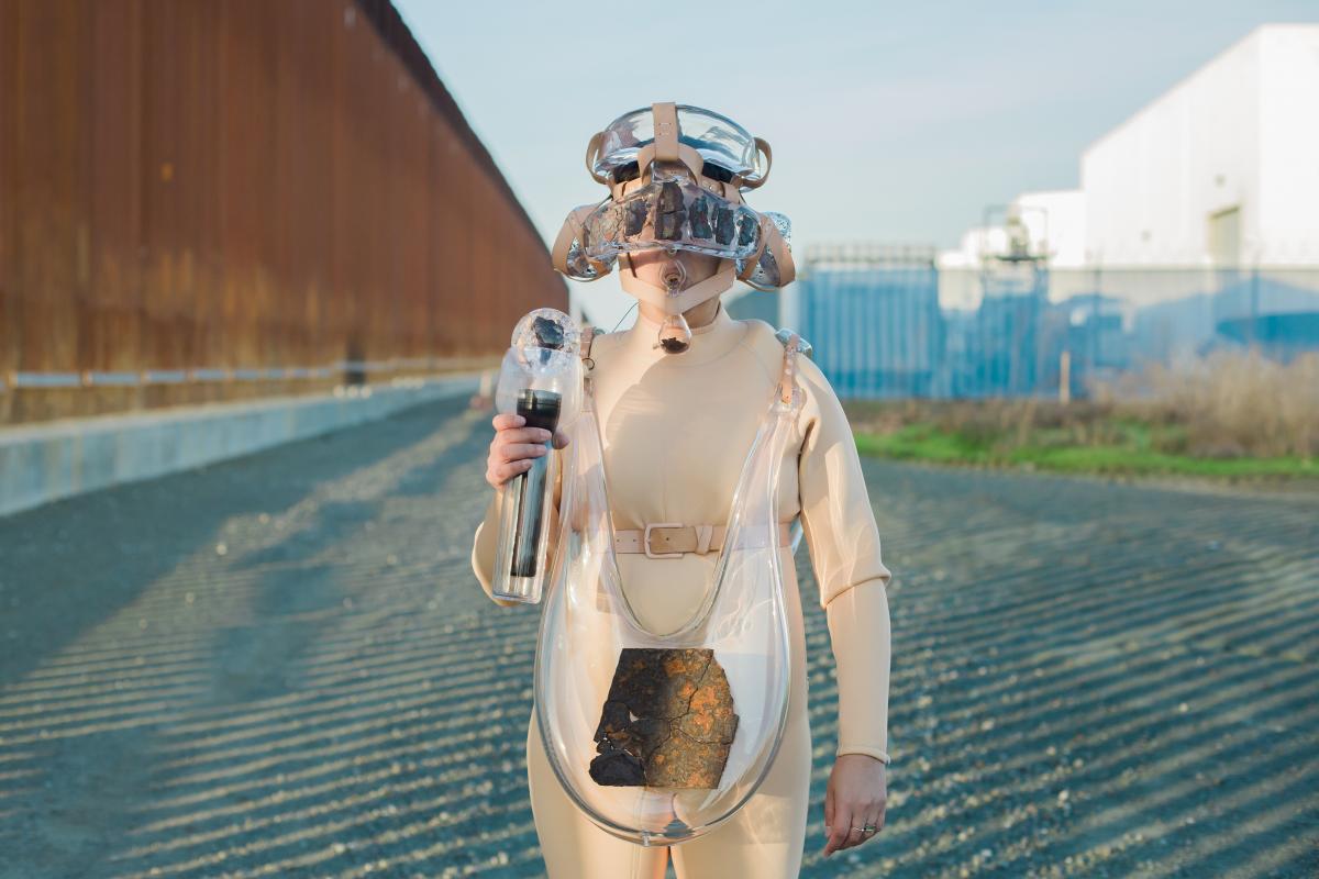 Artist Tanya Aguiñiga wearing a suit made of wearable glass elements at the U.S./Mexico border wall