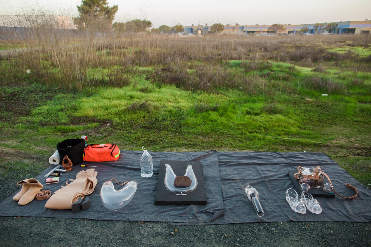 Glass elements of the suit created and worn by artist Tanya Aguiñiga laid out on the grass on top of a black sheet