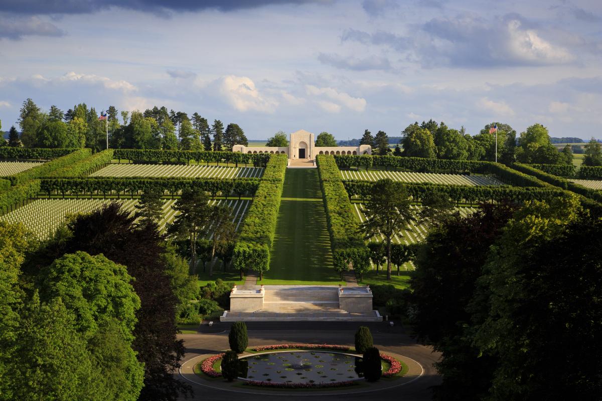 Aerial view of a cemetery with many rows of identical white headstones on either side of a central grassy aisle