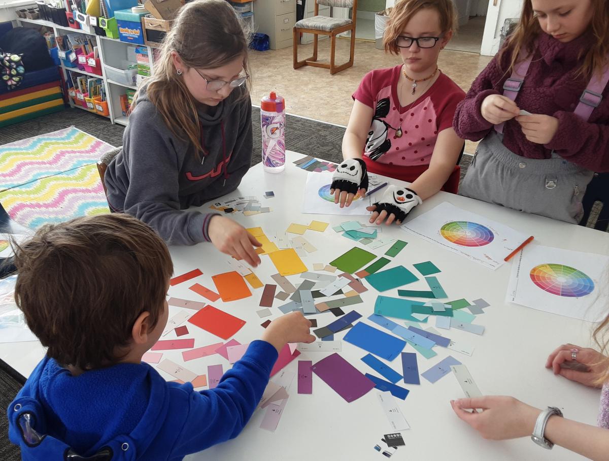 Students in a rural school sit around a table with materials related to a color wheel.