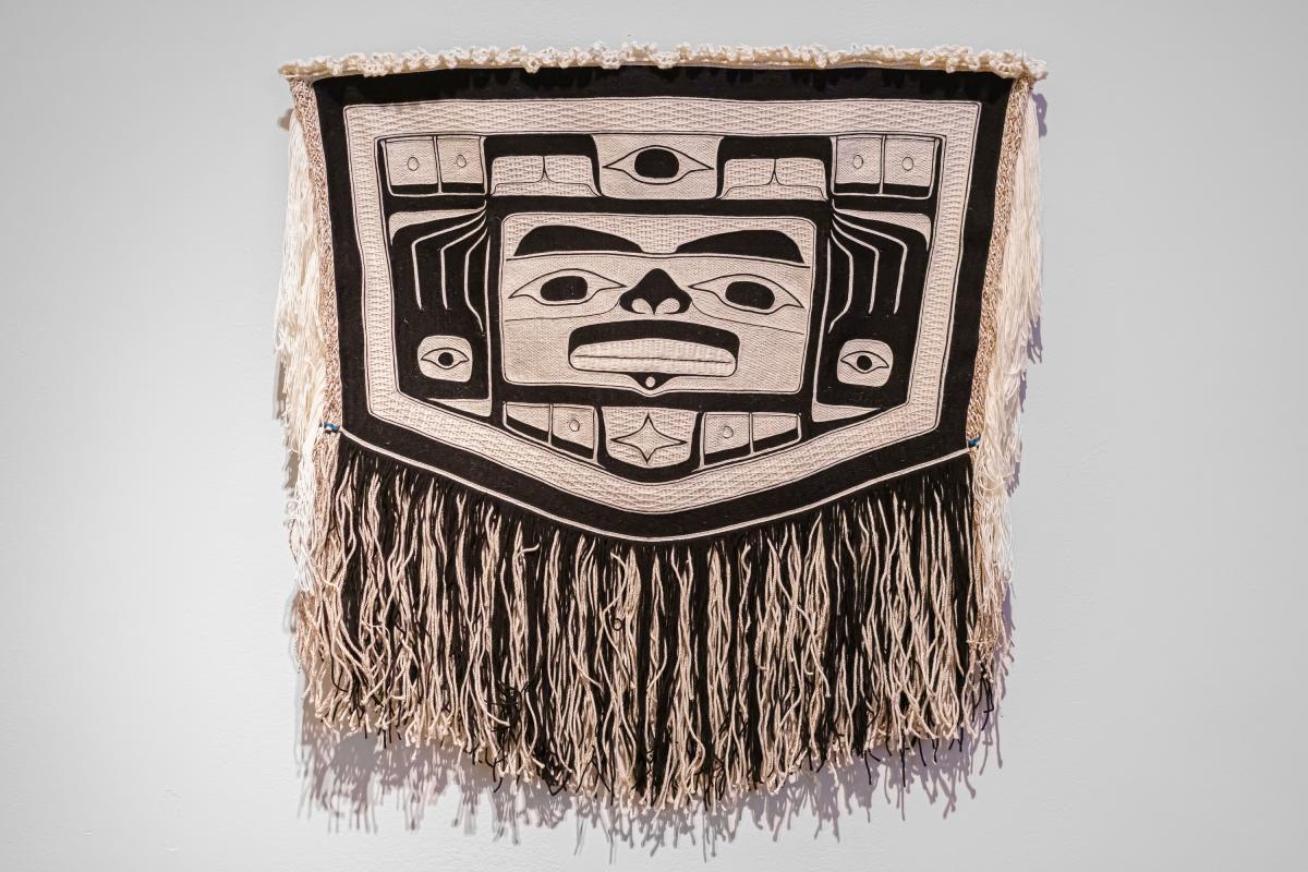 A shawl with traditional Alaskan Native motifs hanging on a gallery wall. 