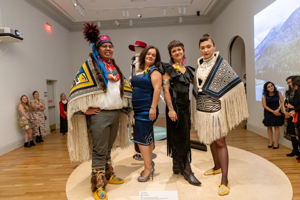 The artists Lily Hope and Ursala Hudson stand with two models, each wearing a blanket with long fringe and Alaska Native motifs.