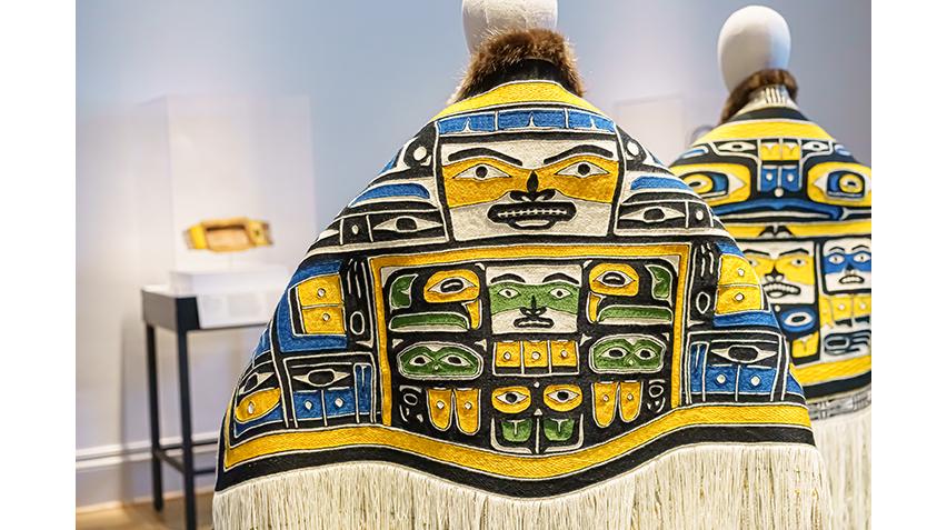 Two traditional robes with traditional Alaskan Native designs side-by-side on mannequins in a gallery.