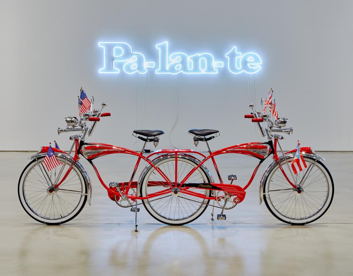 Bicycle sculpture with a neon artwork above it that reads "Pa-lan-te."