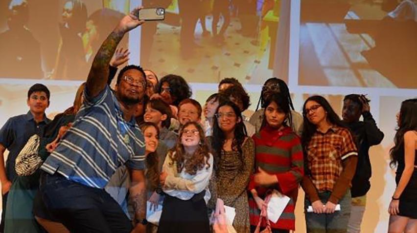 A group of students taking a selfie in front of a projected screen.