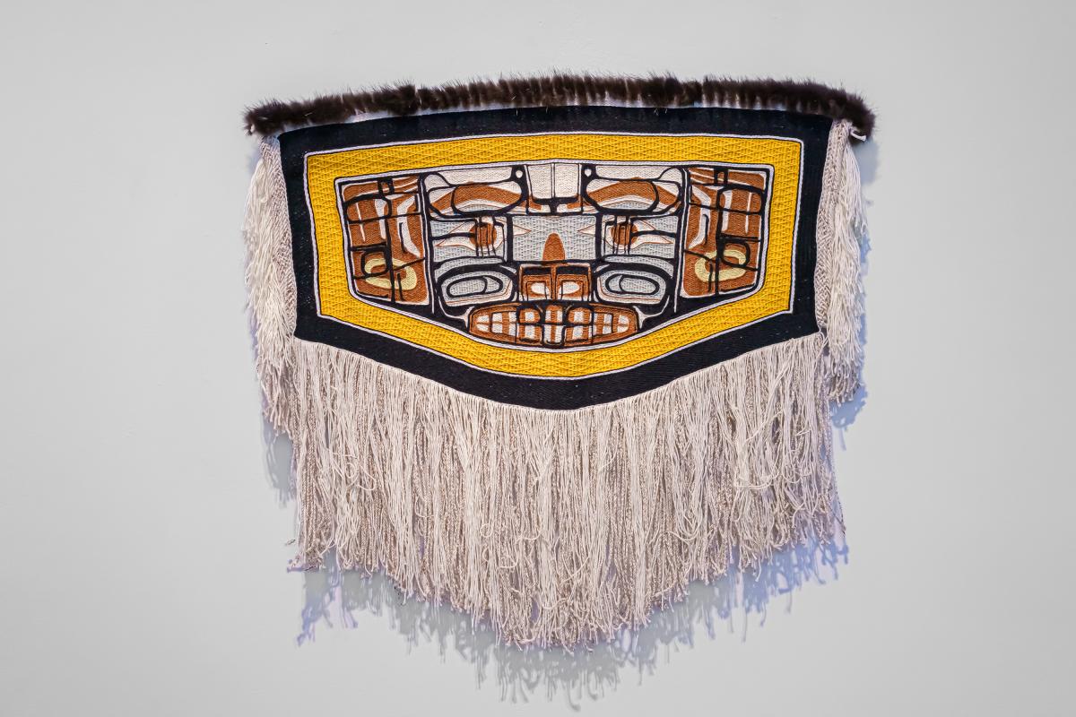 A woven robe with fringe and patterns of brown, blue and white with a yellow border.