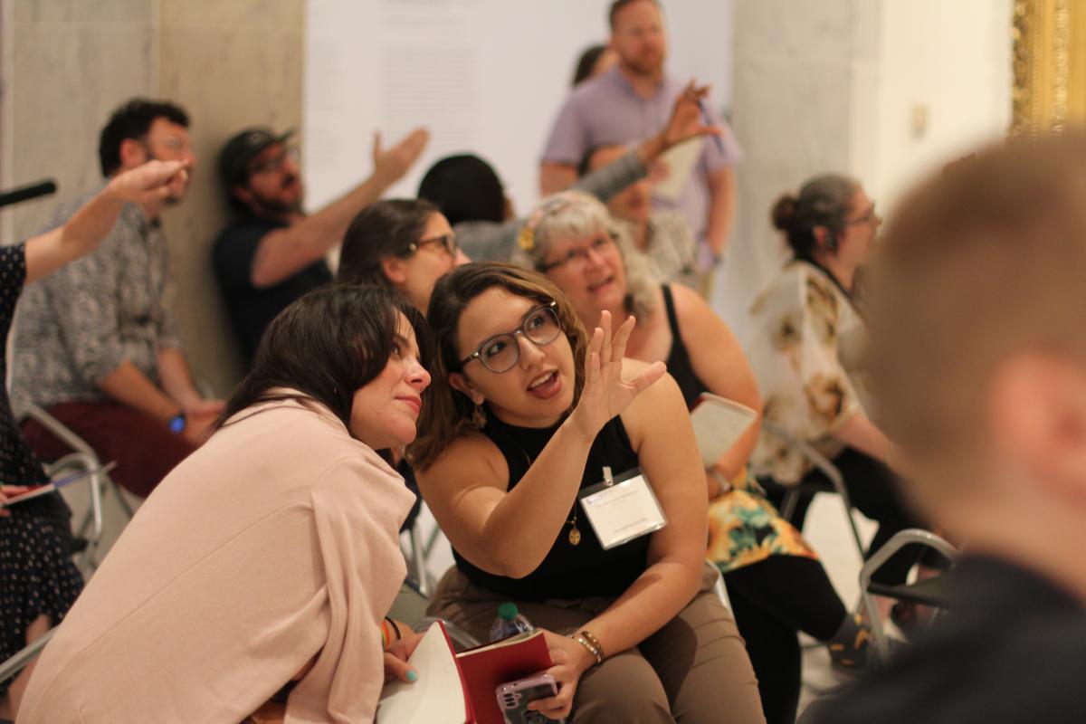  A group of people look and gesture at something outside the frame. They are talking to one another.