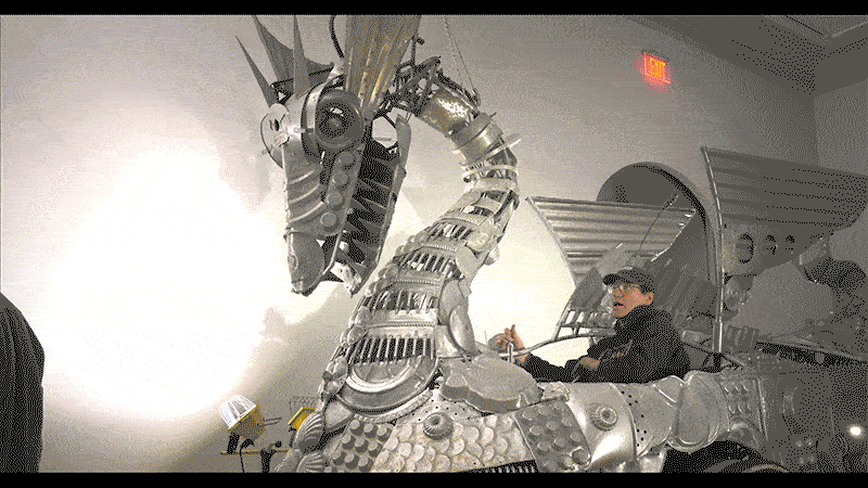 man pulling the levers of a large metallic dragon vehicle