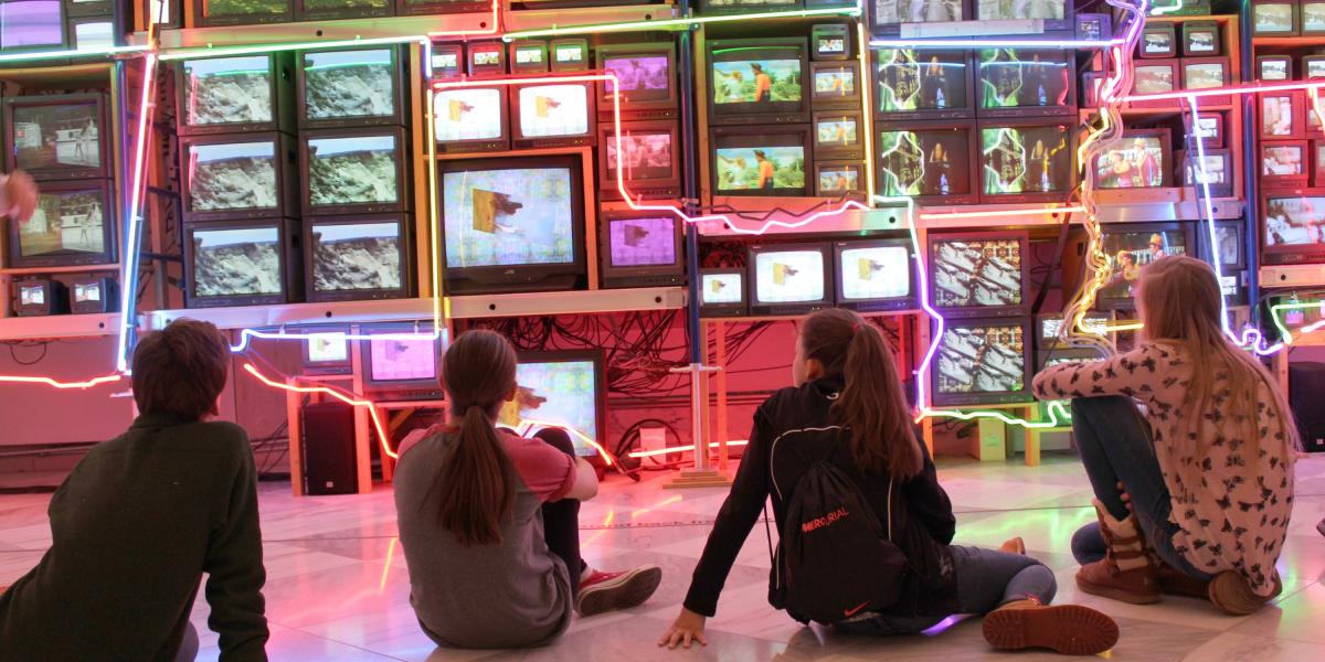 a group of children sit in from of a colorful neon artwork