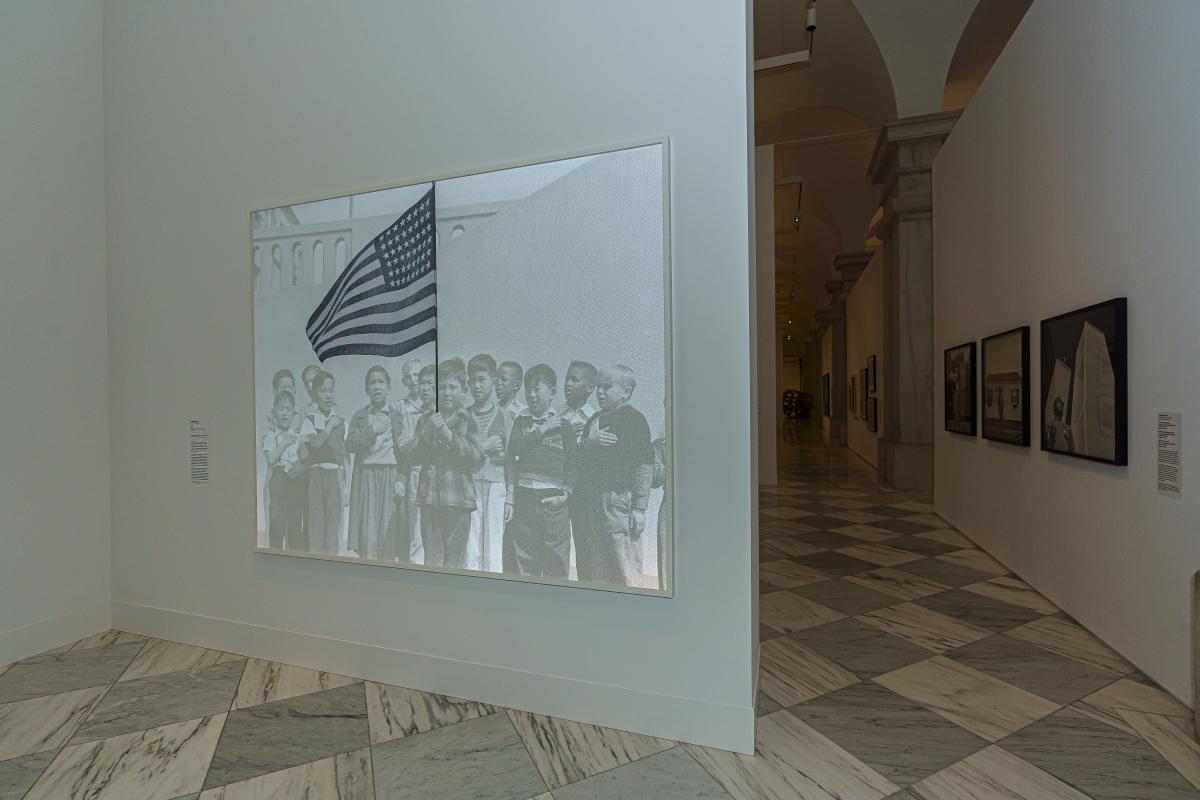 Installation view of a large black and white print of a group of young boys holding a United States flag
