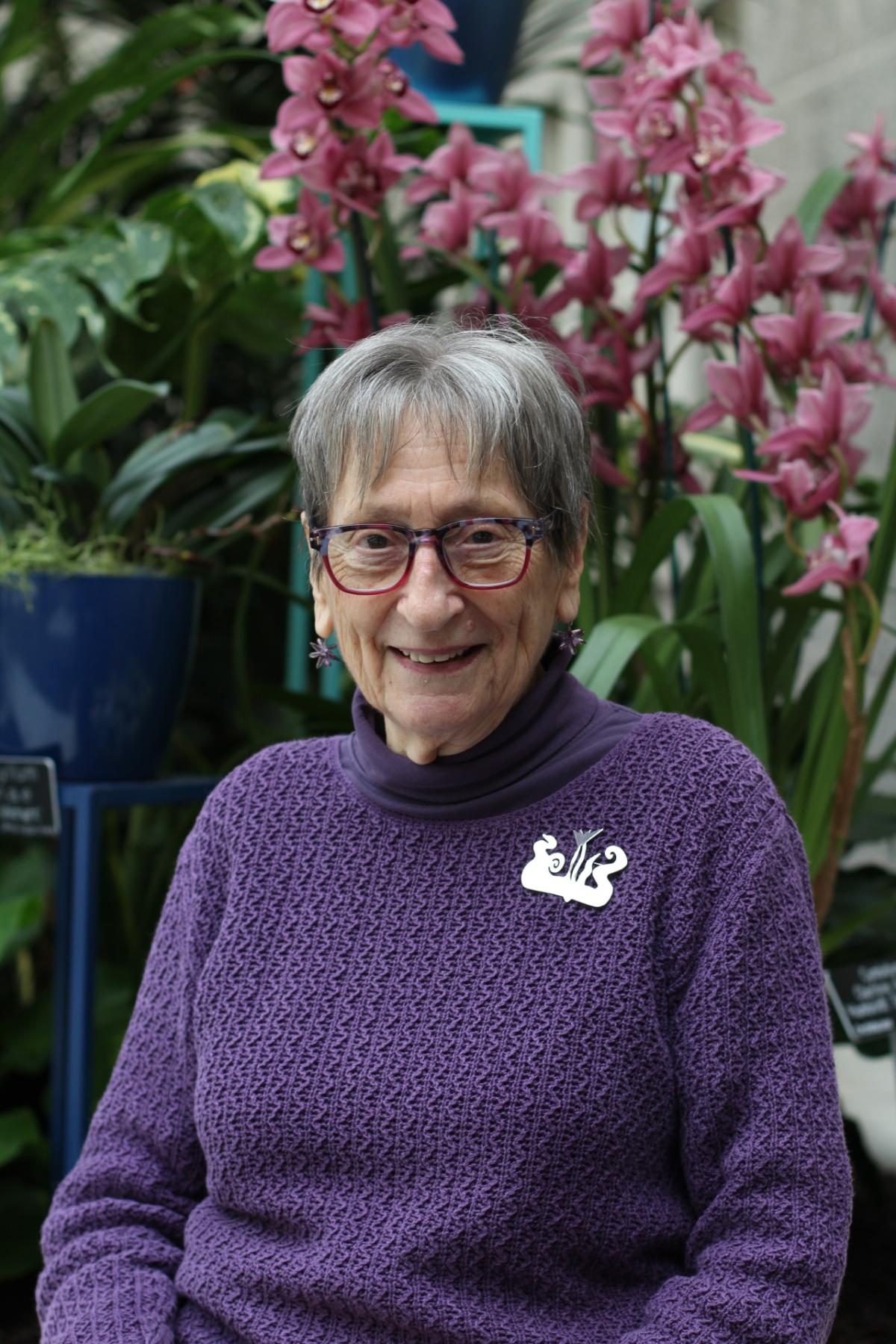 A woman in a purple sweater, gray hair and glasses (and a fabulous Calder inspired pin) sits in SAAM's Kogod Courtyard