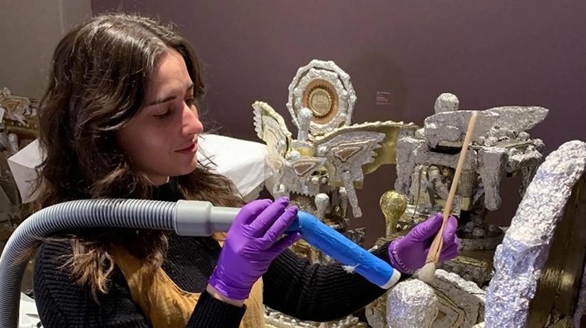 An art conservator holds a vacuum nozzle on a piece of artwork.
