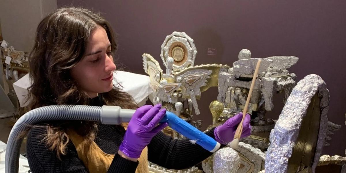 An art conservator holds a vacuum nozzle on a piece of artwork.