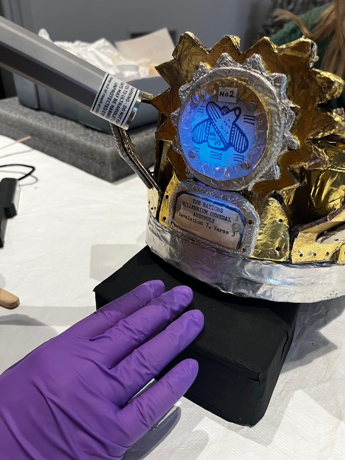 Close up of a component of James Hampton's "Throne," while a conservator is shines a light on it.