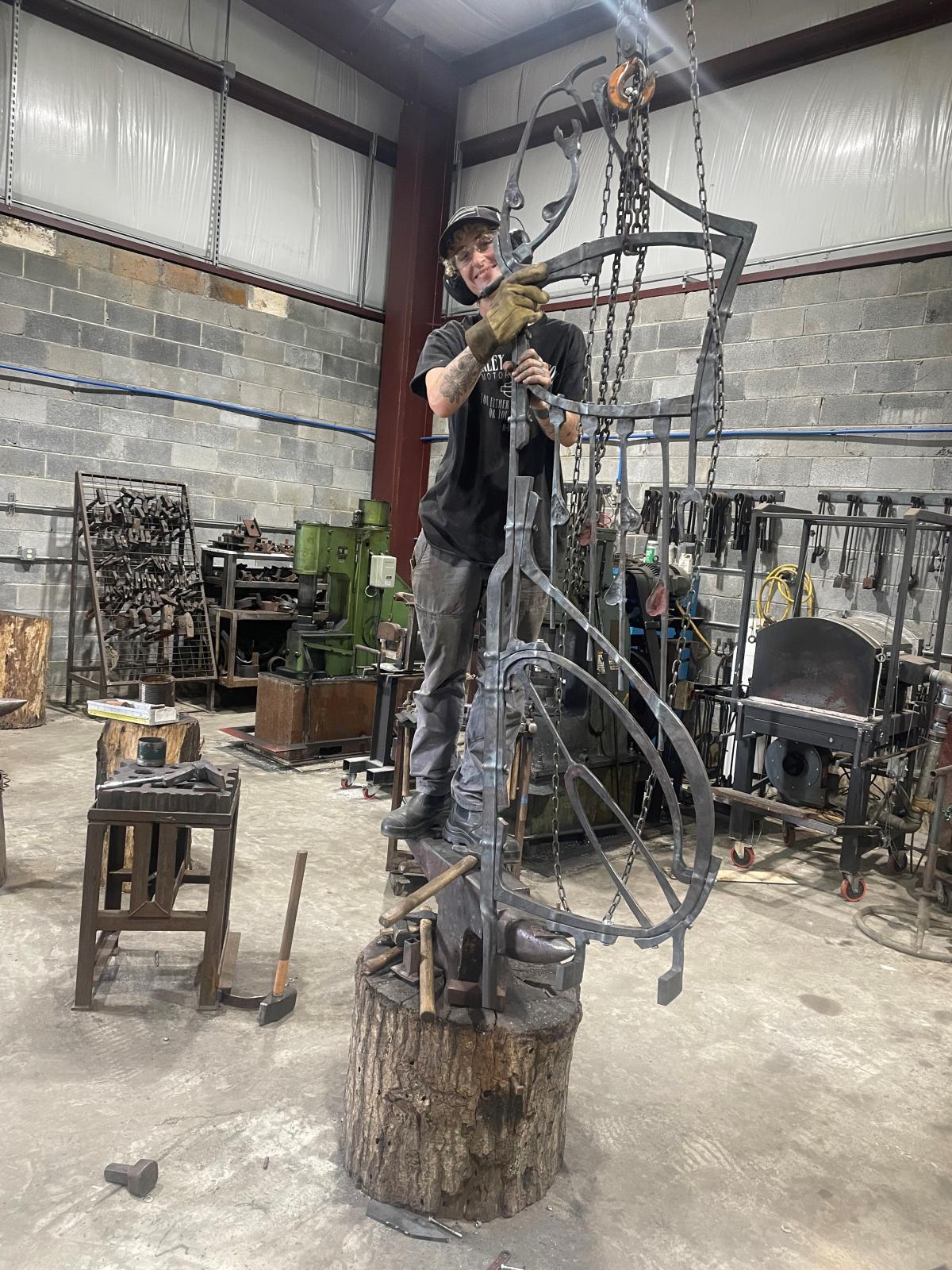 A person stands on a large metal structure in an artist's studio.