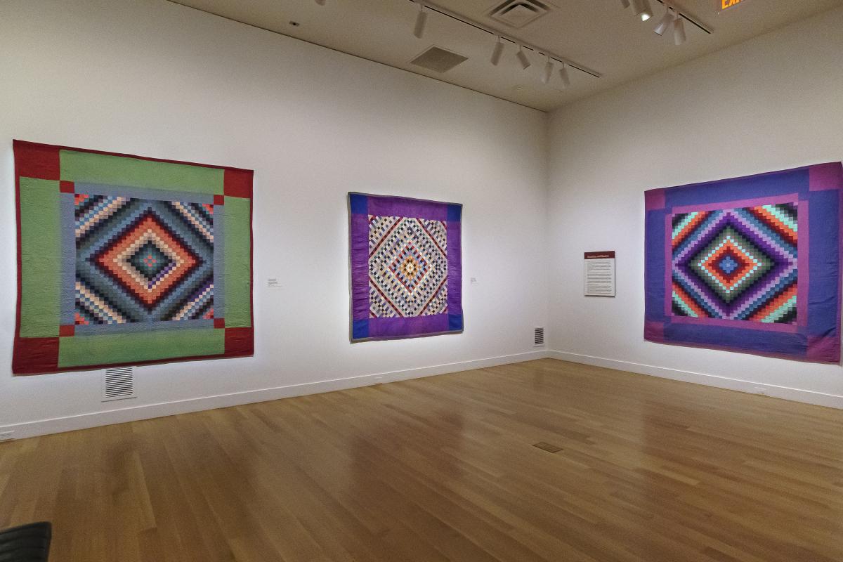 Quilts hang on a gallery wall.