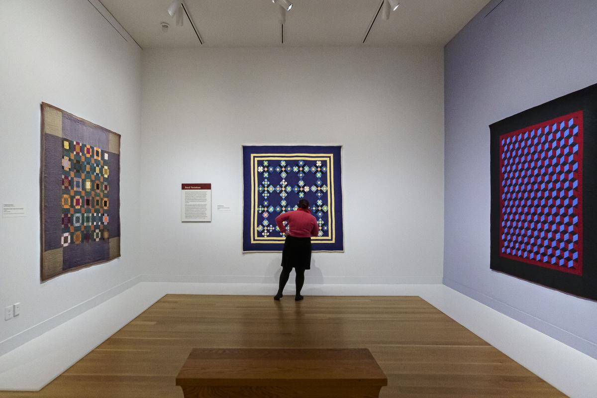 A person stands in front of a quilt hanging in a gallery.