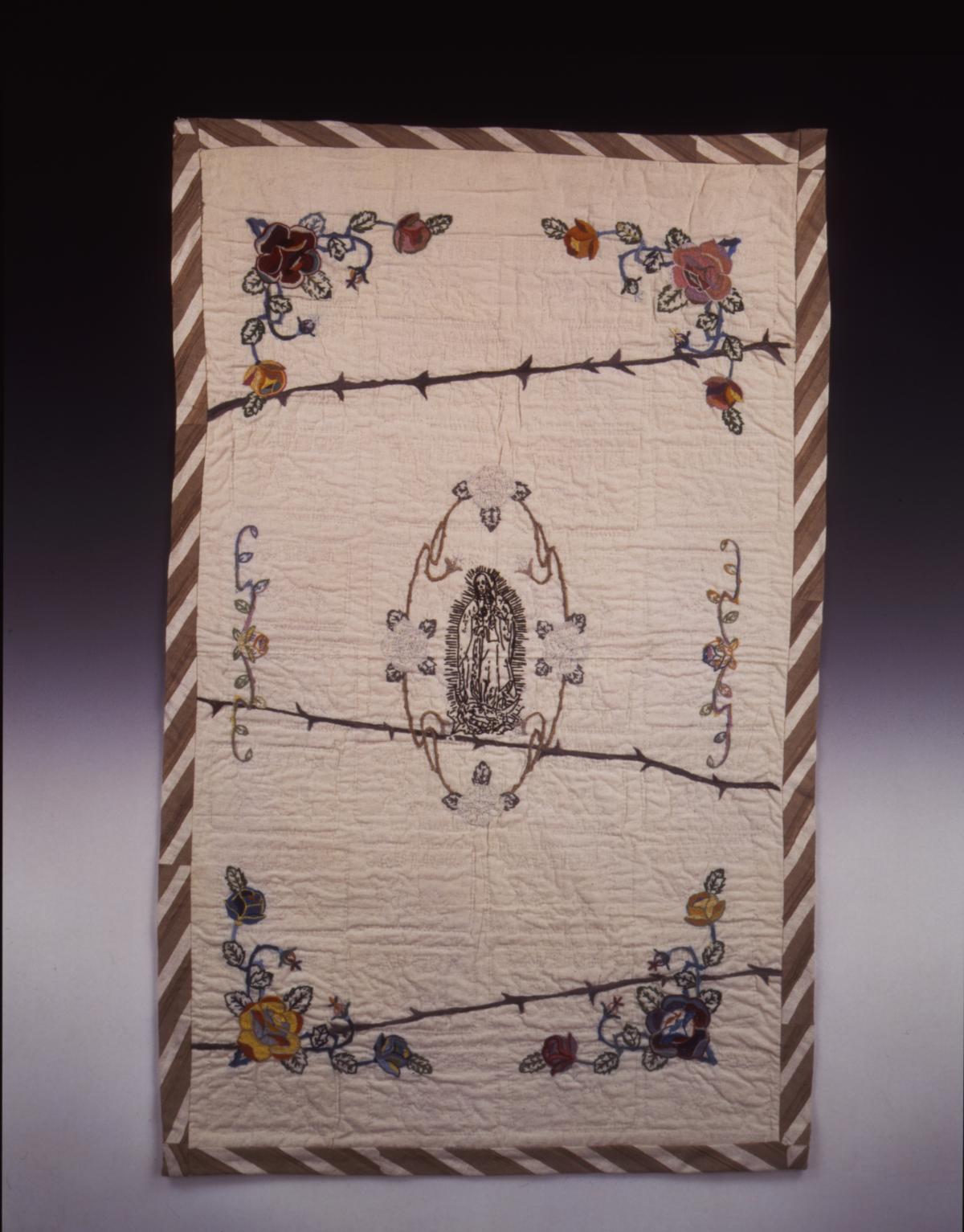 Embroidered tapestry with the Virgen de Guadalupe in the center, flowers around the frame, and barbed wire slashing through the middle of the work.