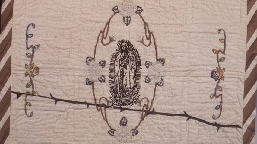 Embroidered tapestry with the Virgen de Guadalupe in the center, flowers around the frame, and barbed wire slashing through the middle of the work.