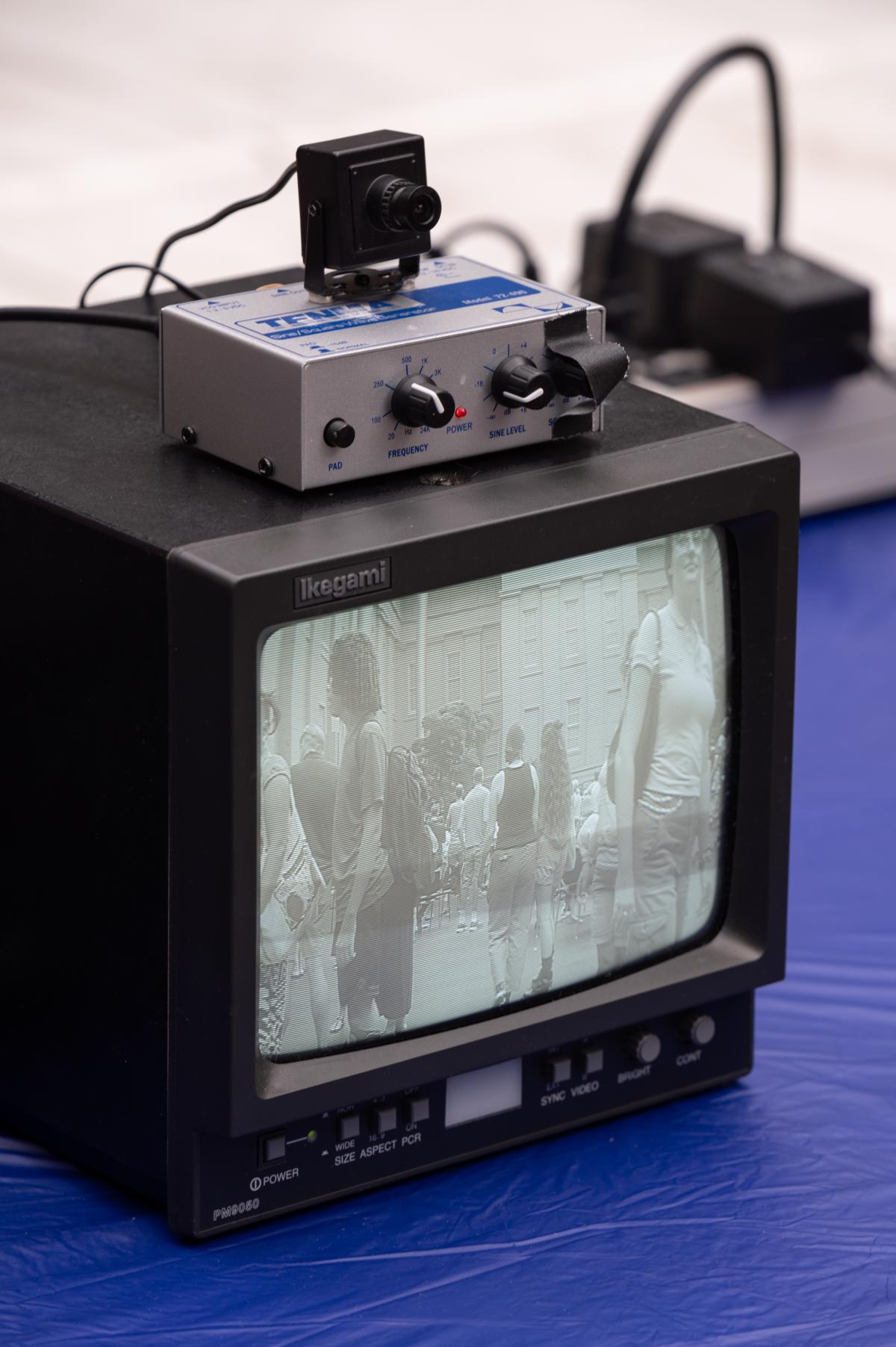 A small black and white tv monitor displays a fuzzy image on the screen. On top of it sits a box with nobs.