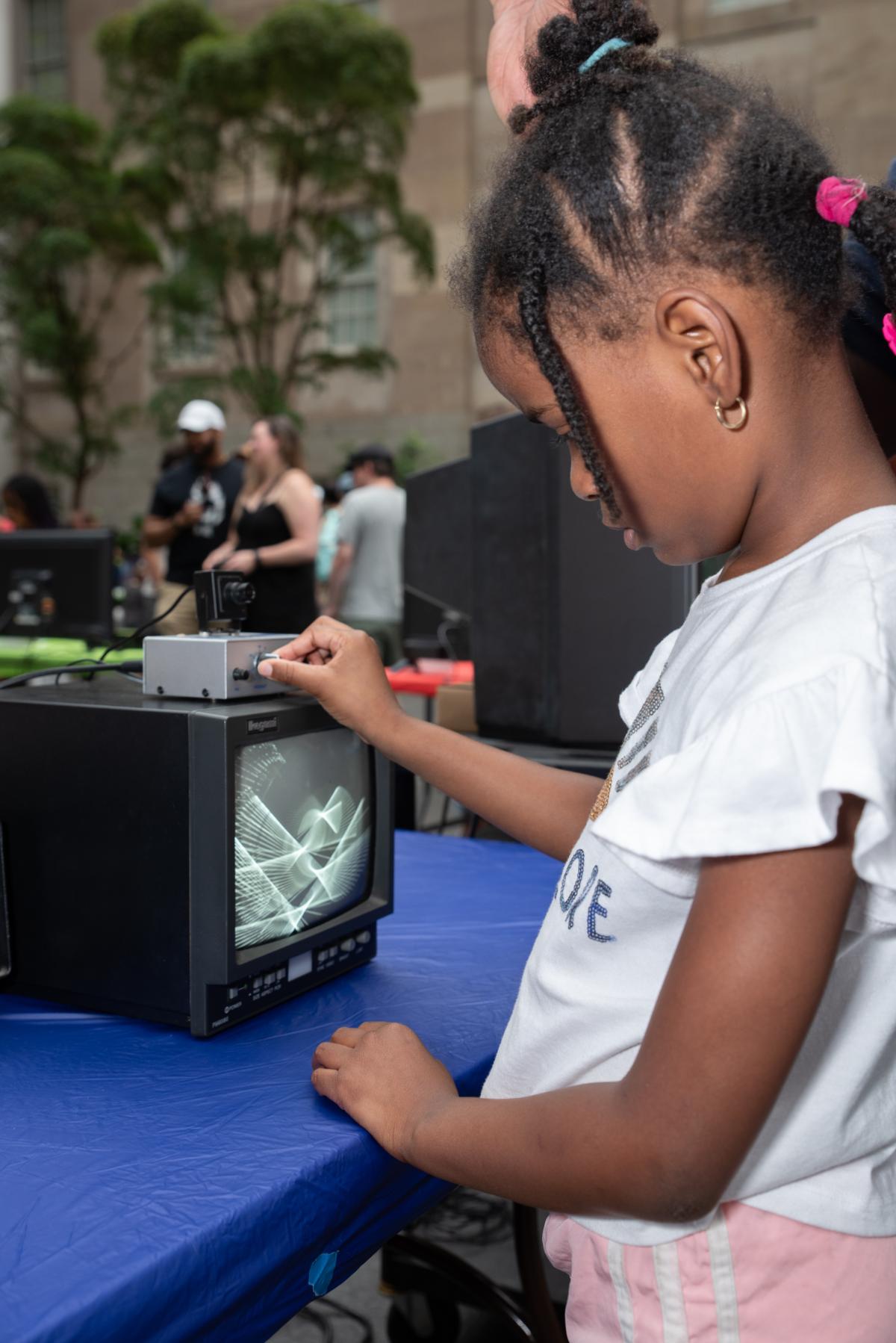 A child turns the nobs of a box sitting atop a small black and white tv monitor.