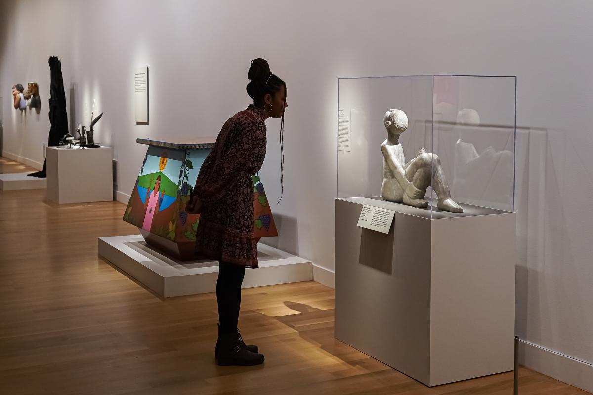 A woman bends over a case to get a better look at a sculpture of a reclining figure.