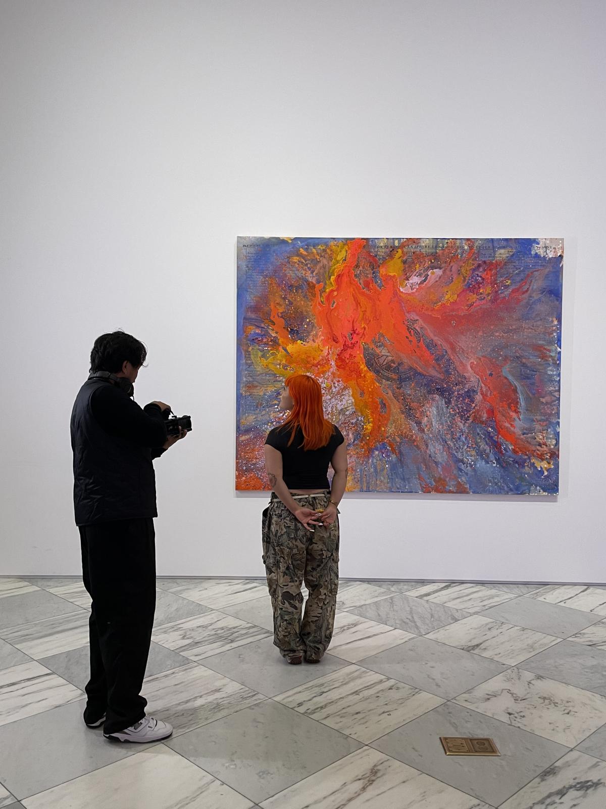 A camera person films a person looking at an abstract painting.